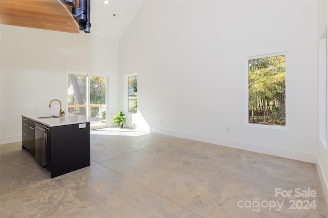 interior space with high vaulted ceiling, stainless steel dishwasher, sink, and a kitchen island with sink