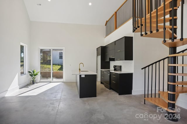 kitchen featuring sink, a breakfast bar, an island with sink, a towering ceiling, and black / electric stove