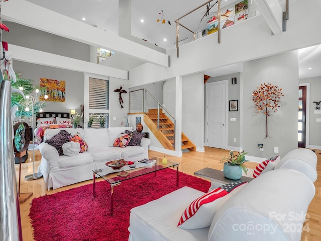 living room featuring wood-type flooring, a towering ceiling, and beam ceiling