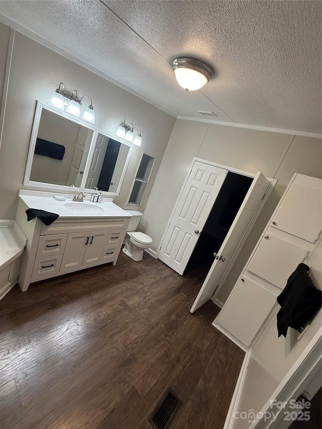bathroom with a textured ceiling, vanity, visible vents, toilet, and wood finished floors