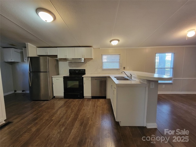 kitchen with a peninsula, appliances with stainless steel finishes, dark wood-style flooring, a sink, and under cabinet range hood
