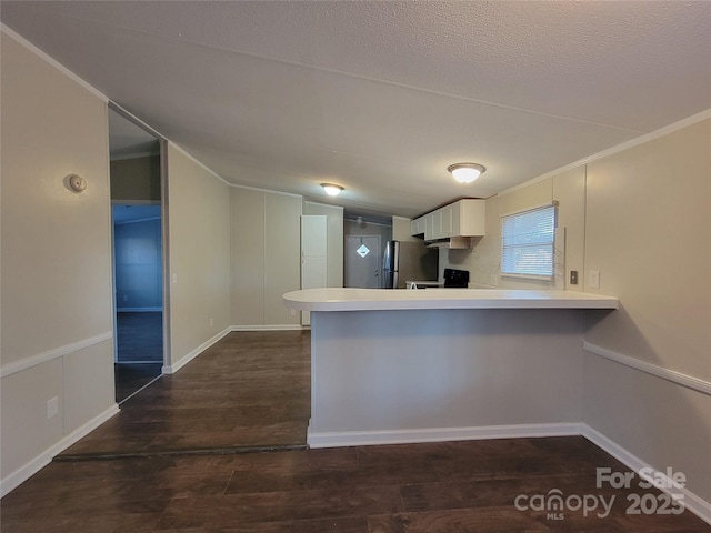kitchen with freestanding refrigerator, dark wood-type flooring, a peninsula, white cabinets, and light countertops