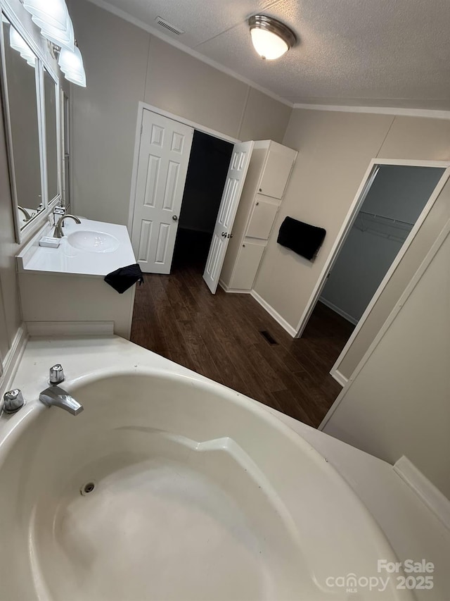 bathroom featuring vanity, ornamental molding, a textured ceiling, visible vents, and wood finished floors