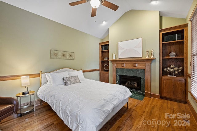 bedroom with wood-type flooring, vaulted ceiling, ceiling fan, and a high end fireplace