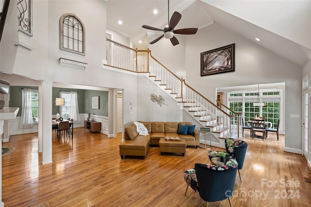 living room with ceiling fan, decorative columns, hardwood / wood-style floors, and high vaulted ceiling