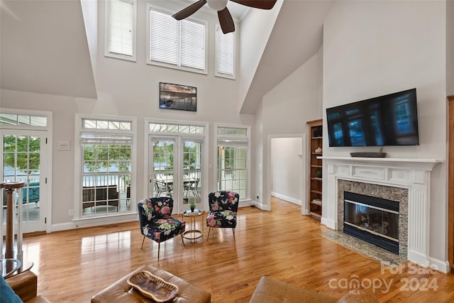 living room with a towering ceiling, light hardwood / wood-style flooring, a fireplace, and ceiling fan