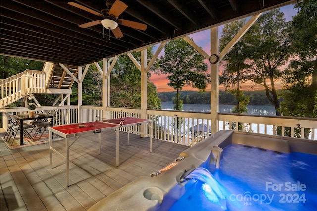 deck at dusk featuring an outdoor hot tub, a water view, and ceiling fan