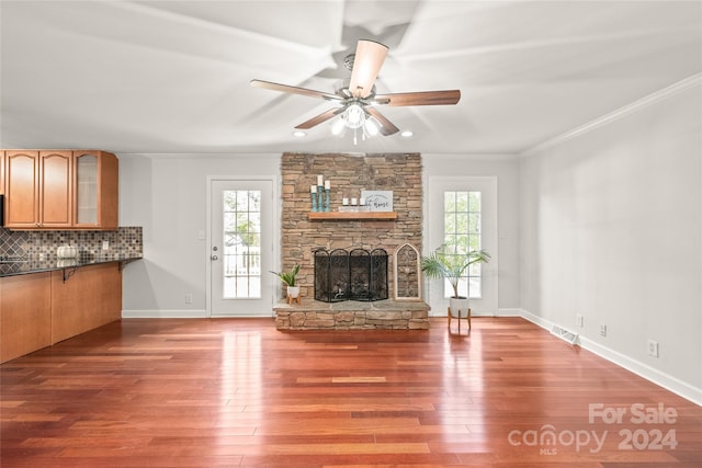 unfurnished living room with ornamental molding, hardwood / wood-style floors, a stone fireplace, and a wealth of natural light