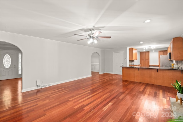 unfurnished living room with crown molding, dark wood-type flooring, and ceiling fan