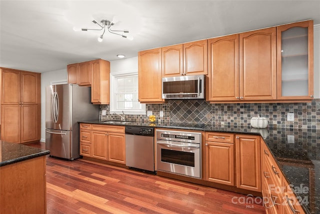 kitchen with decorative backsplash, dark stone countertops, stainless steel appliances, and dark hardwood / wood-style flooring