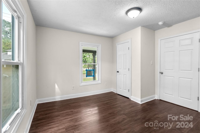 unfurnished bedroom featuring multiple windows, a textured ceiling, and dark hardwood / wood-style floors