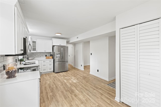 kitchen with backsplash, sink, light hardwood / wood-style flooring, appliances with stainless steel finishes, and white cabinetry