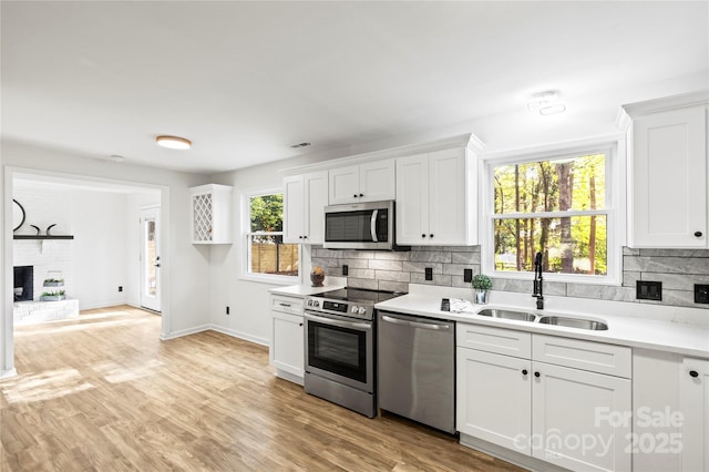 kitchen with sink, a brick fireplace, a healthy amount of sunlight, white cabinetry, and stainless steel appliances