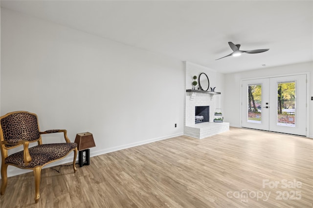 sitting room with a brick fireplace, ceiling fan, french doors, and light hardwood / wood-style flooring