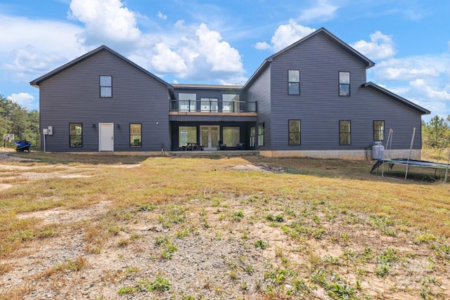 back of property featuring a balcony, a trampoline, and a yard