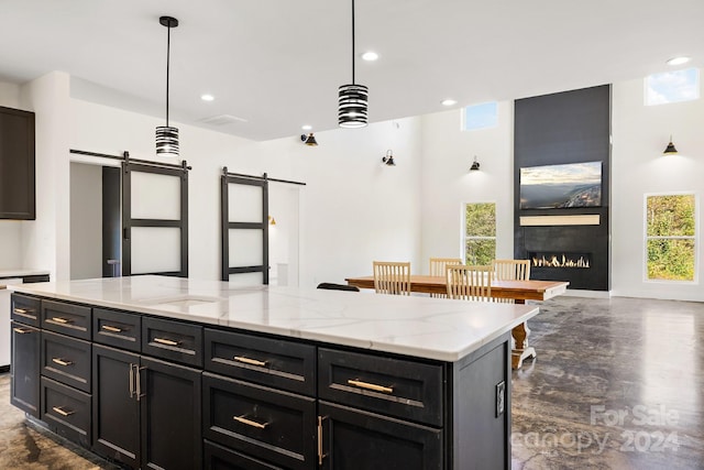 kitchen featuring hanging light fixtures, a kitchen island, a fireplace, light stone countertops, and a barn door