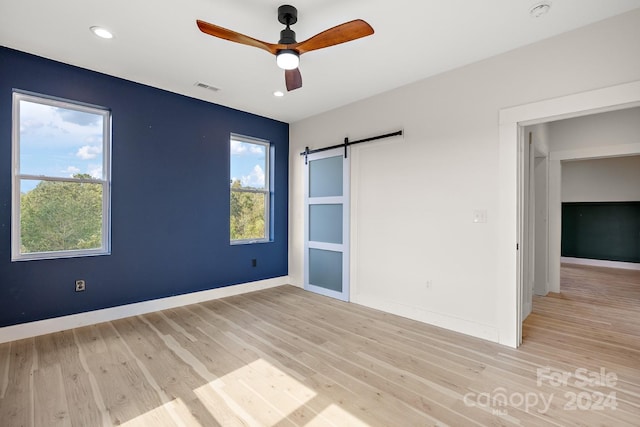 spare room featuring ceiling fan, light wood-type flooring, a barn door, and a wealth of natural light