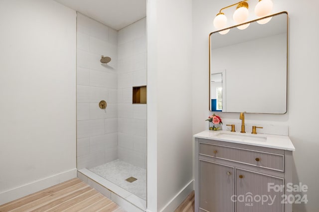 bathroom featuring hardwood / wood-style flooring, a tile shower, and vanity