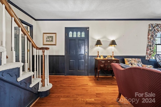 foyer entrance with ornamental molding, wood walls, hardwood / wood-style floors, and a textured ceiling