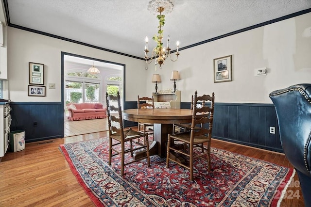 dining room featuring an inviting chandelier, ornamental molding, a textured ceiling, and hardwood / wood-style floors