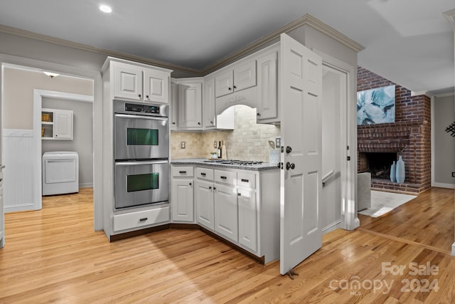 kitchen featuring appliances with stainless steel finishes, light wood-type flooring, ornamental molding, white cabinets, and washer / clothes dryer