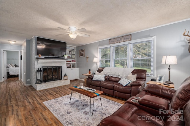 living room with ceiling fan, hardwood / wood-style flooring, a fireplace, crown molding, and a textured ceiling