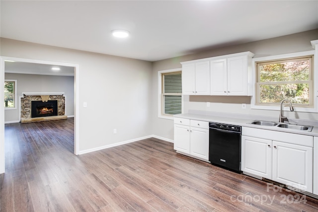 kitchen with white cabinetry, sink, black dishwasher, a stone fireplace, and light wood-type flooring