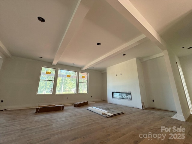 unfurnished living room featuring beamed ceiling, wood finished floors, baseboards, and a glass covered fireplace