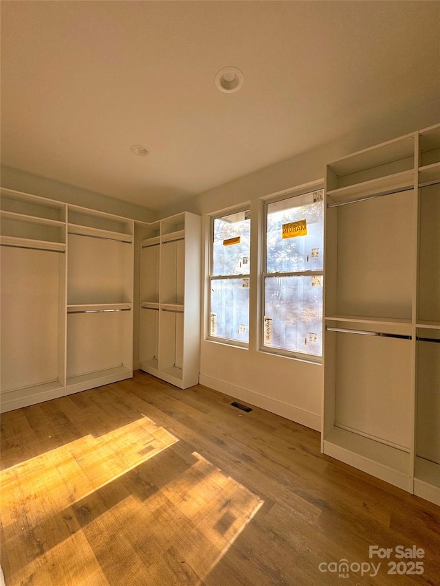 unfurnished bedroom with wood finished floors, visible vents, a closet, and baseboards