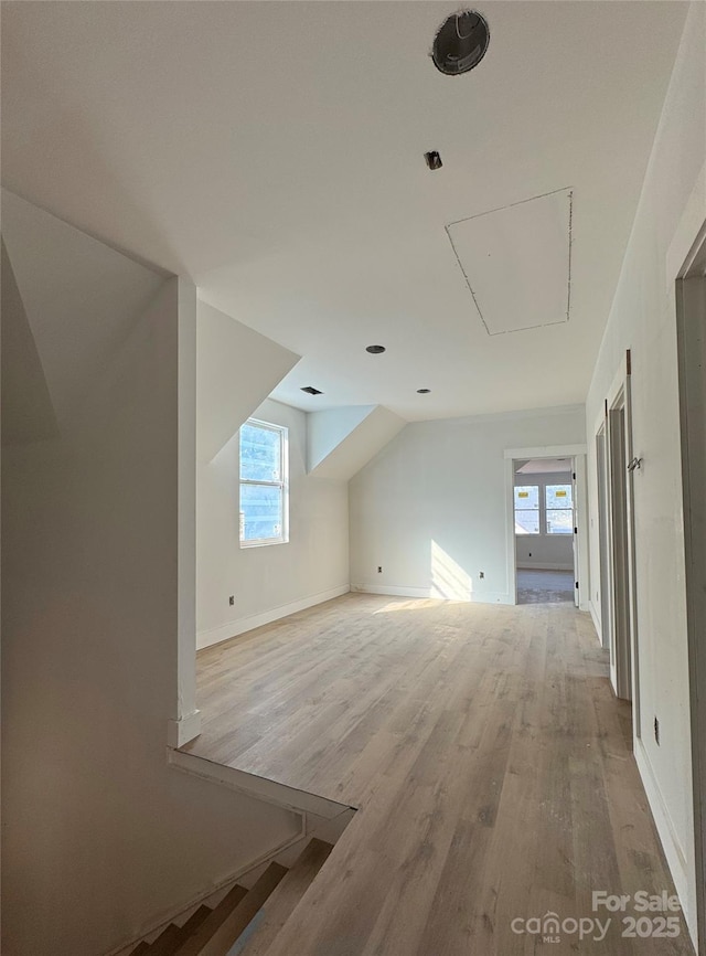 bonus room featuring baseboards, attic access, light wood-type flooring, and lofted ceiling