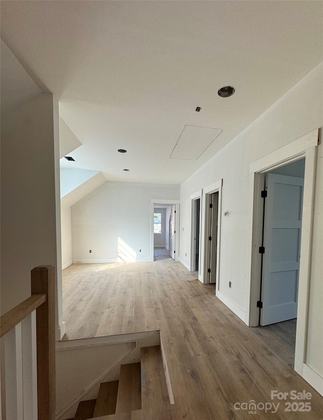 hall with vaulted ceiling, an upstairs landing, wood finished floors, and baseboards