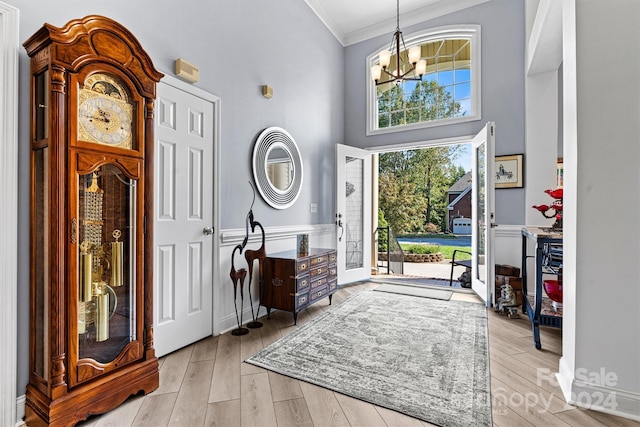 foyer entrance featuring a chandelier, light wood finished floors, a towering ceiling, and ornamental molding
