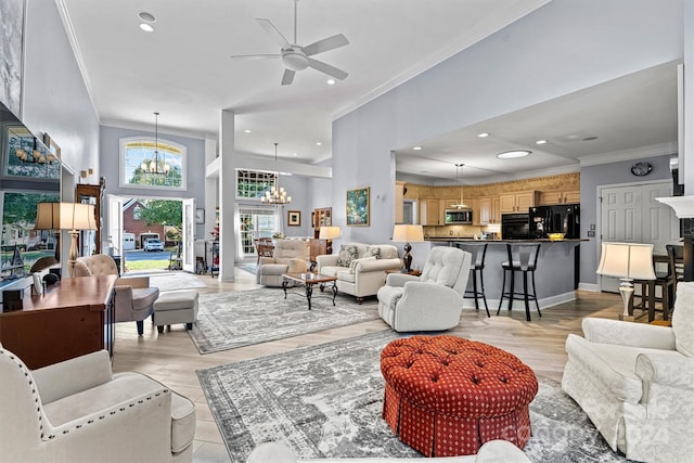 living room featuring ceiling fan with notable chandelier, light hardwood / wood-style floors, a towering ceiling, and ornamental molding