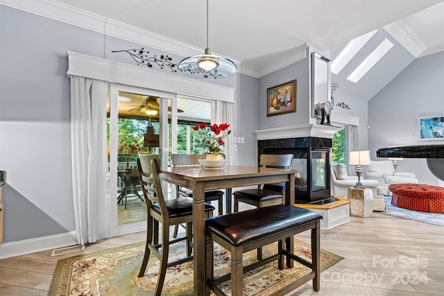 dining area with vaulted ceiling with skylight, ornamental molding, a multi sided fireplace, and light hardwood / wood-style flooring