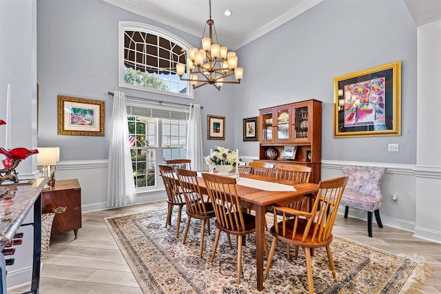 dining room featuring a towering ceiling, light wood-style floors, crown molding, baseboards, and a notable chandelier