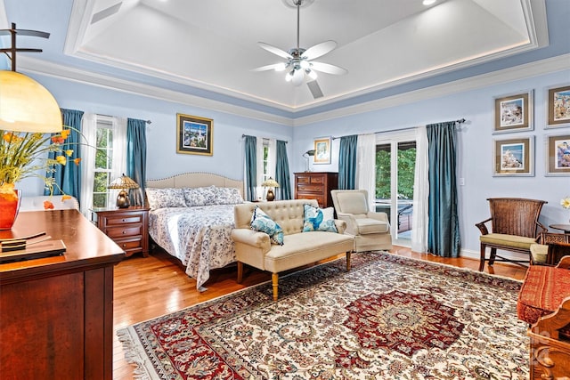 bedroom with crown molding, a tray ceiling, light wood-type flooring, and ceiling fan