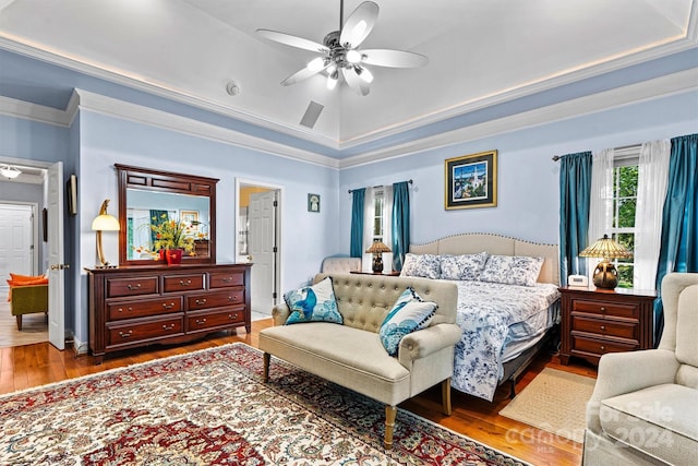 bedroom with ceiling fan, wood finished floors, ornamental molding, and a tray ceiling