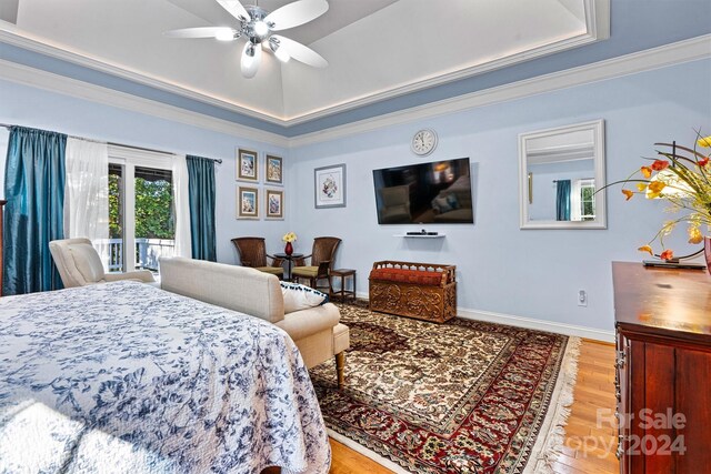 bedroom with ceiling fan, light hardwood / wood-style floors, a tray ceiling, ornamental molding, and access to exterior