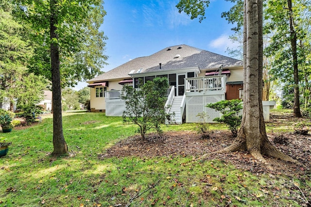 rear view of property featuring stairway, roof with shingles, a wooden deck, a lawn, and a sunroom