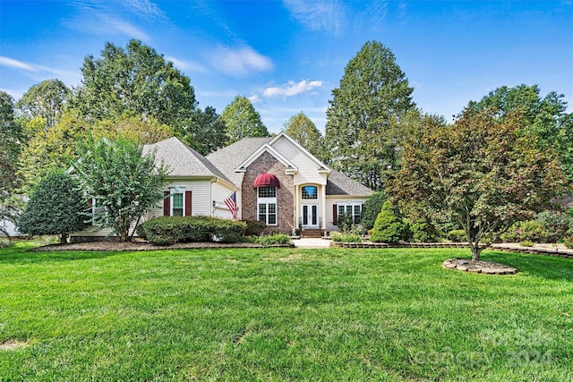 view of front facade with brick siding, french doors, a shingled roof, and a front yard