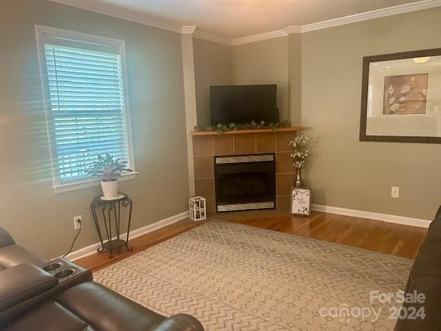living room with a tiled fireplace, baseboards, ornamental molding, and wood finished floors