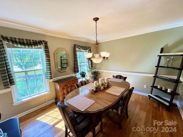 dining space with ornamental molding, wood-type flooring, and an inviting chandelier