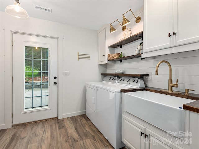 clothes washing area with wood-type flooring, separate washer and dryer, cabinets, and sink