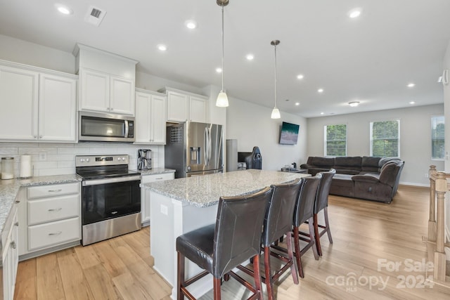 kitchen with white cabinets, stainless steel appliances, light wood-style flooring, and backsplash