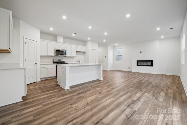 kitchen with range, a center island with sink, sink, light hardwood / wood-style floors, and white cabinetry