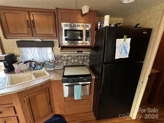 kitchen featuring light wood-type flooring, stainless steel microwave, sink, backsplash, and black refrigerator