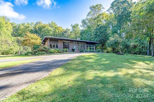 single story home featuring a front lawn, driveway, and a wooded view