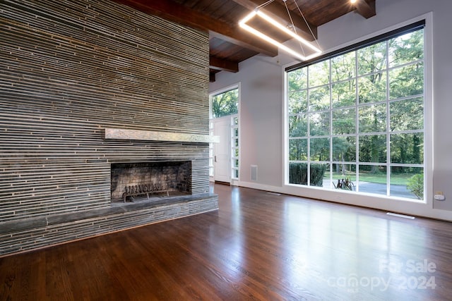 unfurnished living room with baseboards, beamed ceiling, a fireplace with raised hearth, dark wood-style floors, and visible vents