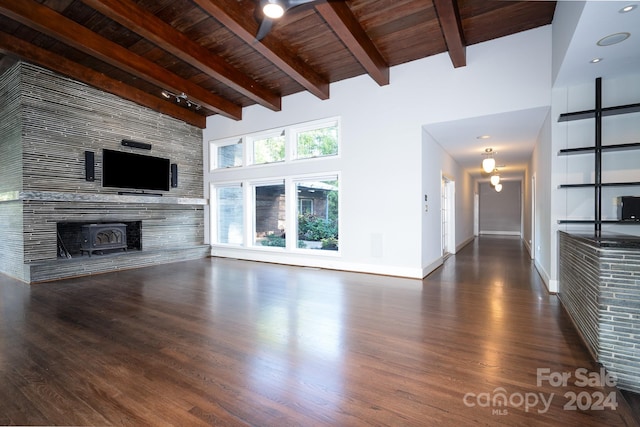 unfurnished living room with wood ceiling, a towering ceiling, a wood stove, and dark hardwood / wood-style flooring