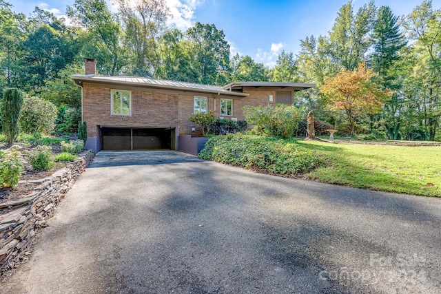 view of front of home featuring a chimney, a standing seam roof, a garage, driveway, and a front lawn